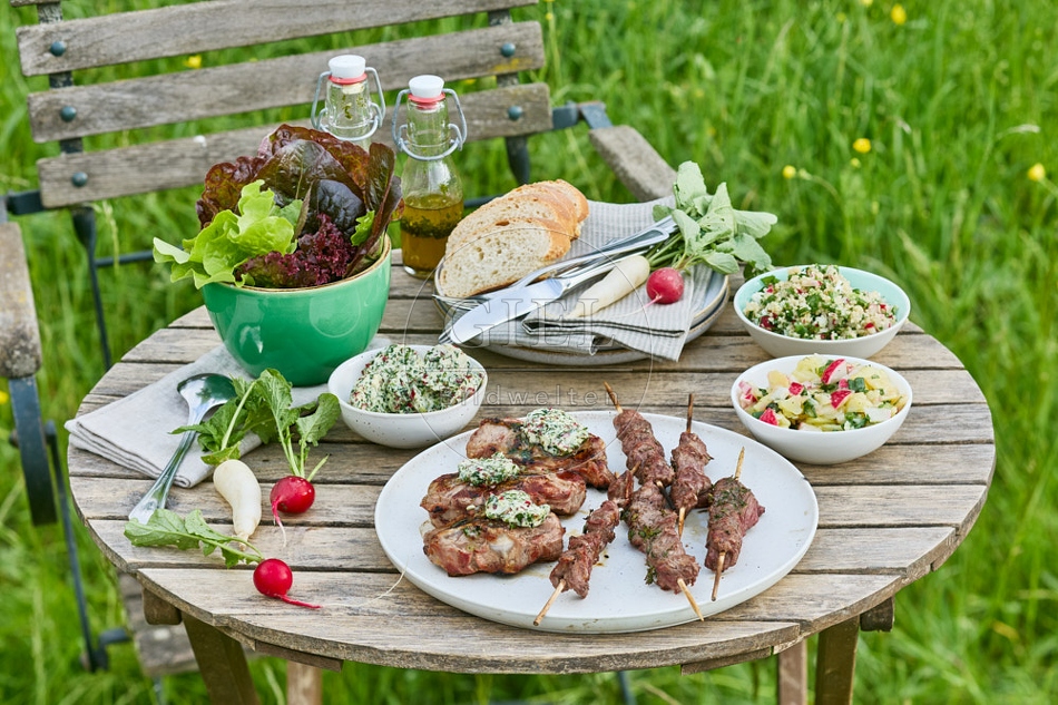 116721 Gedeckter Gartentisch mit gegrilltem Fleisch und Salaten