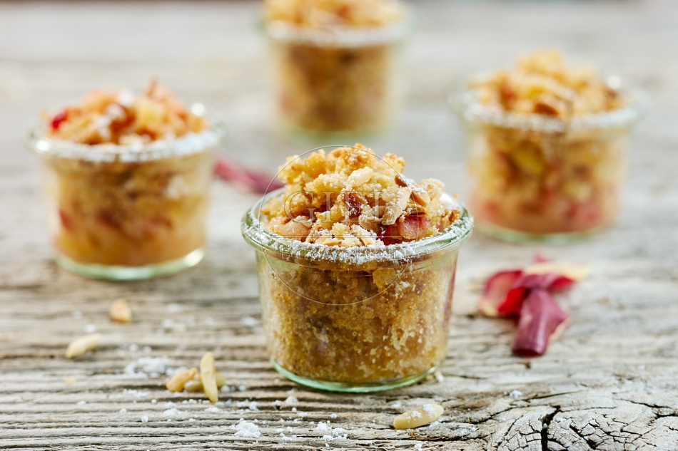 118135 Vier hausgemachte Apfelcrumbles in Gläsern auf rustikalem Holztisch