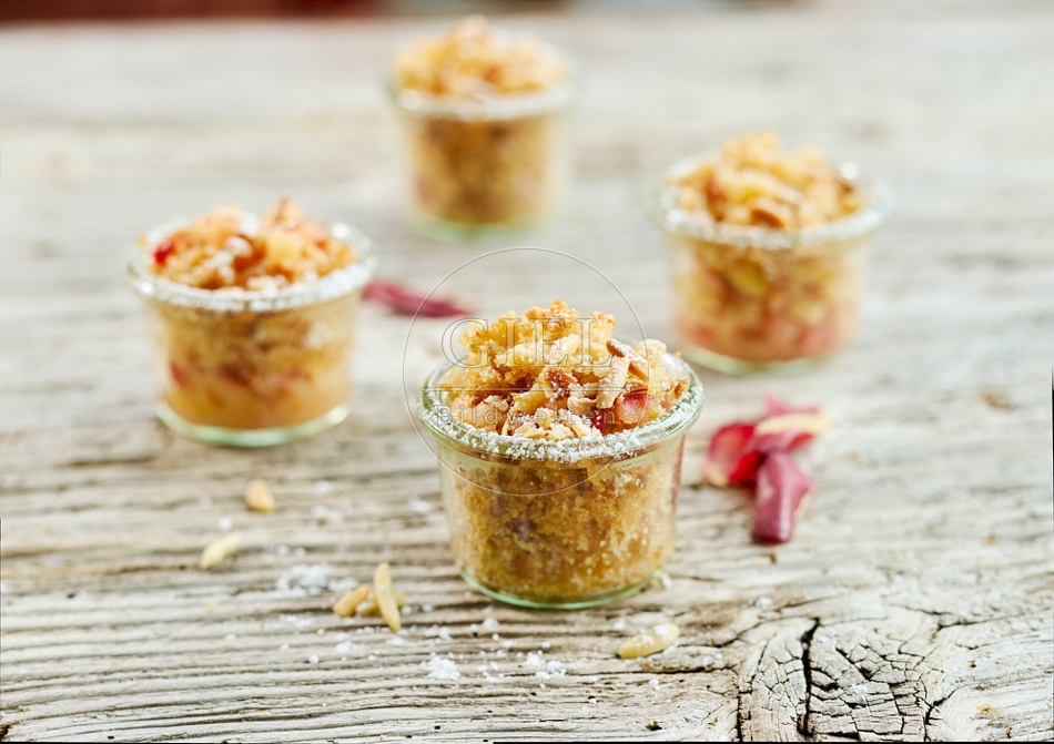 118136 Vier hausgemachte Apfelcrumbles in Gläsern auf rustikalem Holztisch